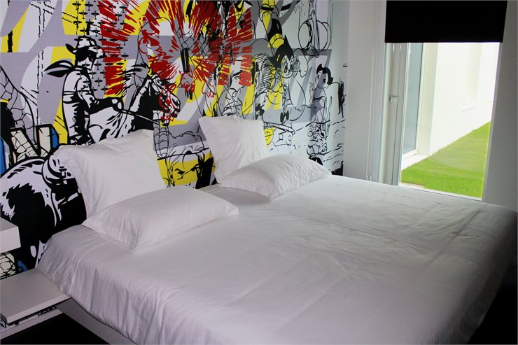 Белоснежная кровать на фоне ярко расписанной стены в Design & Wine Hotel